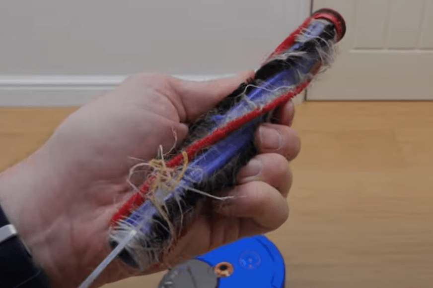 Stark verschmutze Hauptbürste eines Saugroboters wird von Haaren befreit.